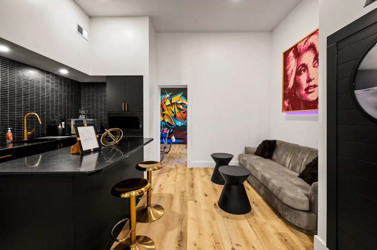 A modern kitchen with a black countertop, gold bar stools, and a wooden floor.