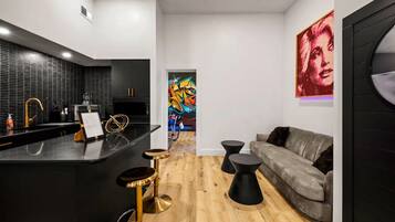 A modern kitchen with a black countertop, gold bar stools, and a wooden floor.