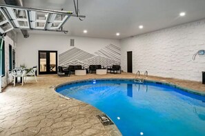 An indoor swimming pool with a geometric wall design, seating area with chairs and tables, and a visible door.