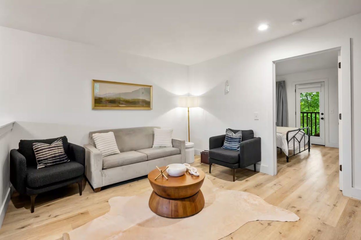 Una sala de estar moderna con un sofá, sillones, una mesa de centro y un cuadro en la pared.
