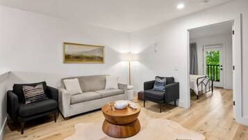 Una sala de estar moderna con un sofá, sillones, una mesa de centro y un cuadro en la pared.