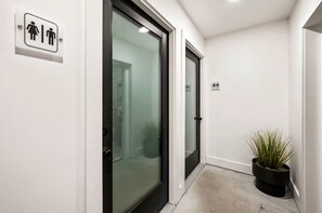 A hallway with a glass door, a potted plant, and a restroom sign.