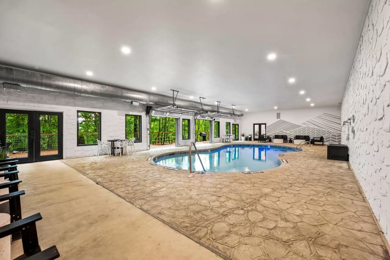 An indoor swimming pool with a stone floor, surrounded by windows and chairs.