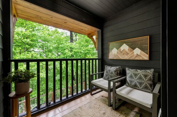 A balcony with a wooden railing, a seating area with cushions, and a painting on the wall.