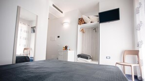 Une chambre à coucher avec un lit, un téléviseur fixé au mur, une chaise et une armoire.