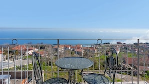 Un balcon avec une balustrade en métal, une table ronde en verre et deux chaises.