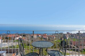 Un balcone con ringhiera in metallo, un tavolino rotondo in vetro e due sedie.