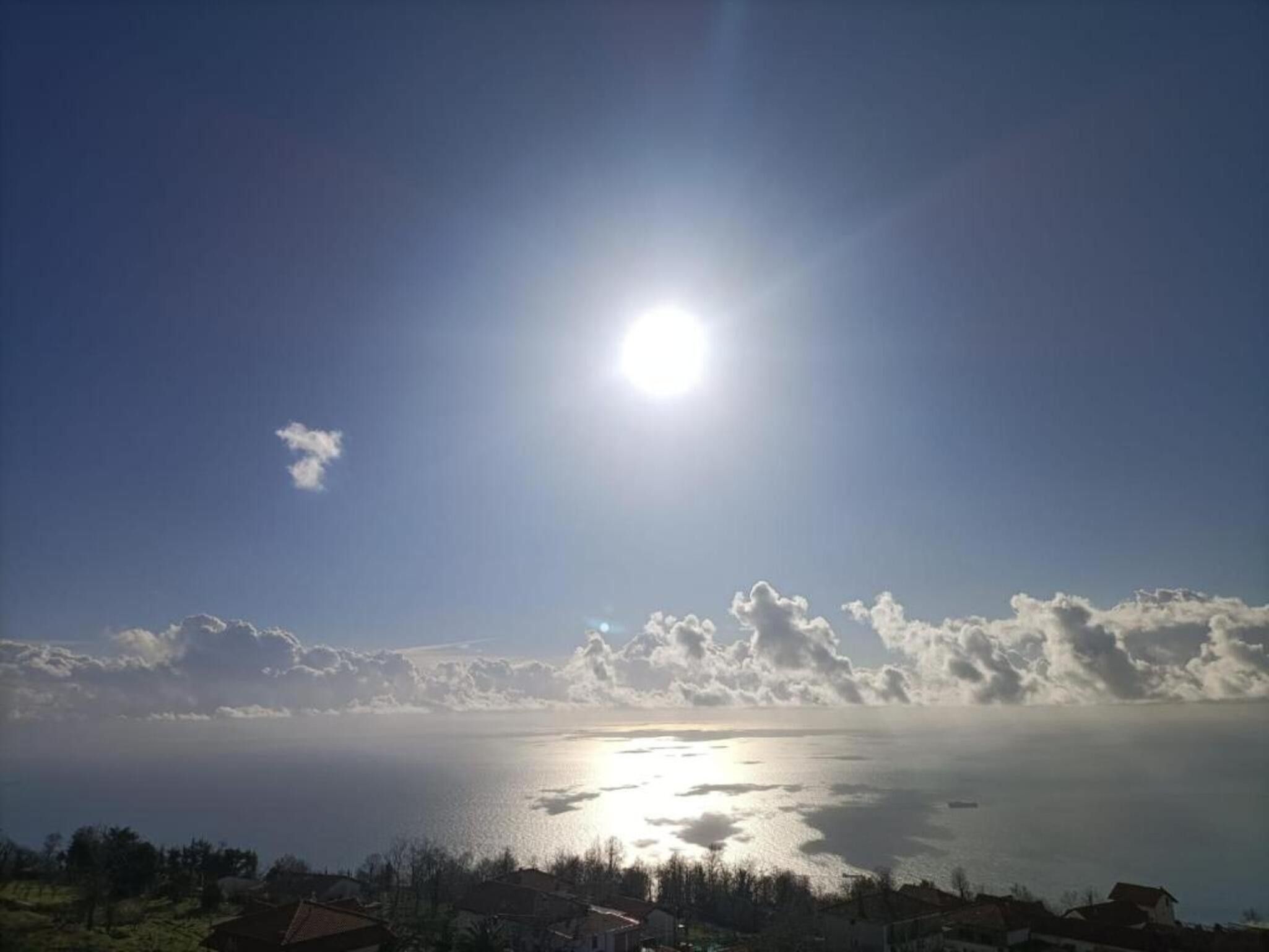 A coastal view with a clear sky, a bright sun, and a calm sea.