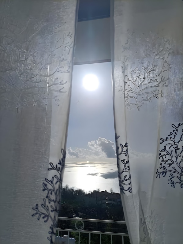 Una finestra con vista sul cielo e nuvole, incorniciata da una tenda con motivi floreali.