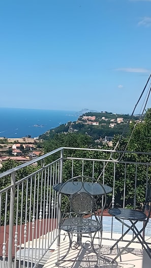 Un balcone con una sedia e un tavolo in metallo, affacciato su un paesaggio costiero con case e barche.