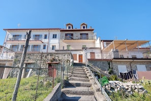 A multi-story building with a staircase leading to a door, surrounded by vegetation and a fence. - Room 'Camera Sogno' with Sea View, Wi-Fi and Air Conditioning (Pianillo)