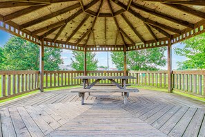 Un belvédère en bois abritant une table de pique-nique au centre, entouré d’une terrasse en bois et de rampes.