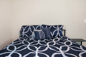 A bed with a geometric patterned bedspread and pillows, a bedside table, and a plain wall. - Misty Lane Retreat | Walk to Parks & Disc Golf (Ashland)