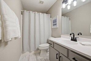 Une salle de bain avec un lavabo blanc, un robinet noir et un rideau de douche.