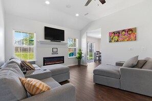 A spacious living room with a fireplace, grey sofas, a flat-screen TV, and a colorful artwork on the wall. - Penny Lane Retreat | 15 Min. to Stadium (Columbia)