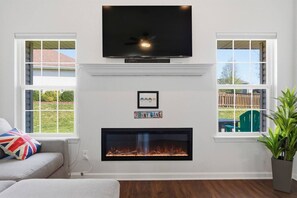 A living room with a fireplace, a flat-screen TV mounted above it, and a sofa with a flag pillow. - Penny Lane Retreat | 15 Min. to Stadium (Columbia)