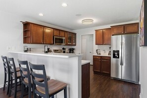 A modern kitchen with wooden cabinets, a stainless steel refrigerator, and a bar area with chairs. - Penny Lane Retreat | 15 Min. to Stadium (Columbia)