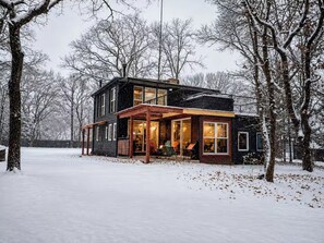 Una casa a due piani con un portico coperto, circondata da alberi innevati.