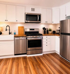 A modern kitchen with stainless steel appliances, white cabinetry, and a wooden floor. - Spacious 4-bedroom house in peaceful Texoma (Kingston)