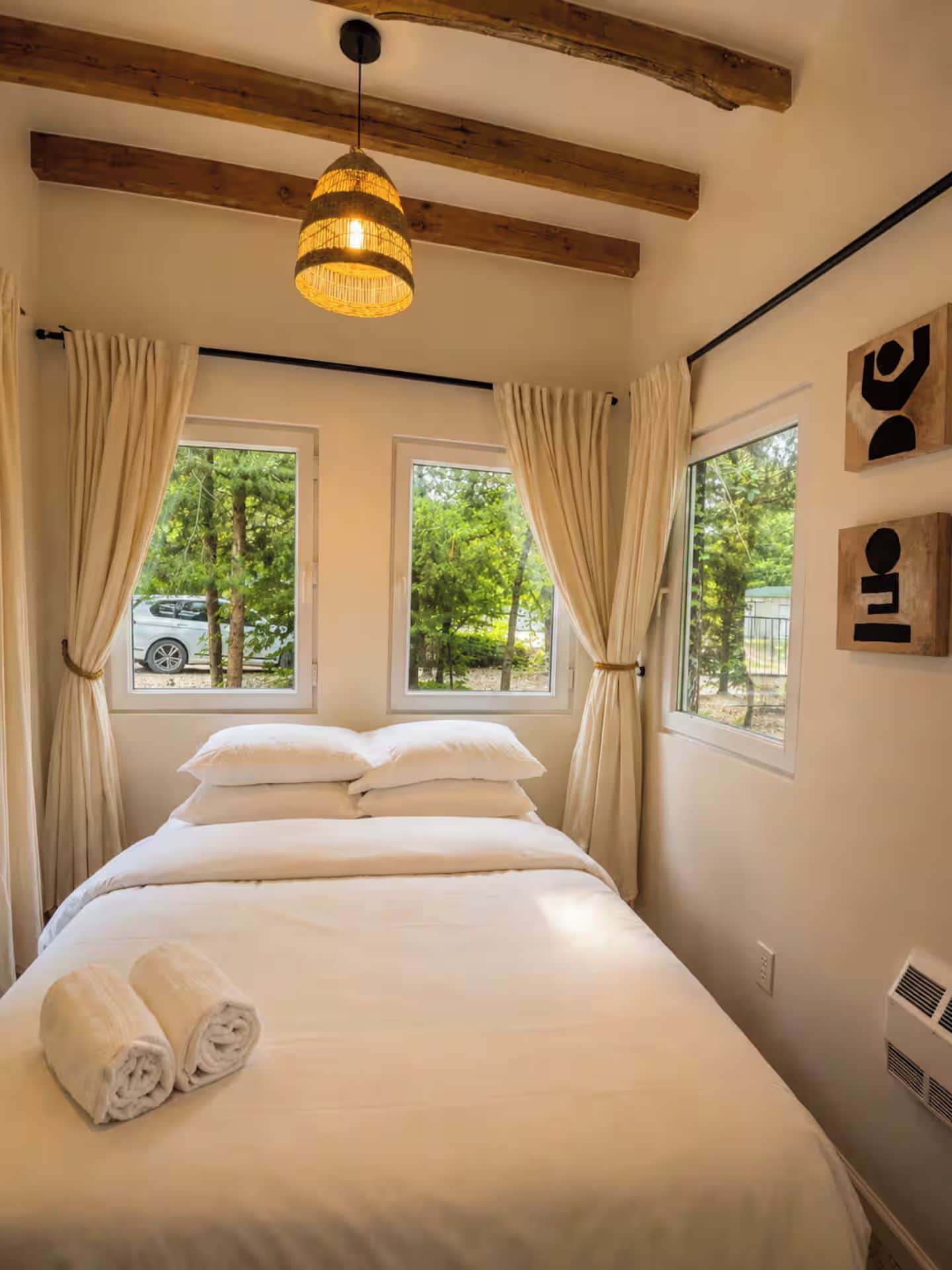 Un dormitorio con una cama, dos ventanas, una lámpara colgante y un respiradero en la pared.