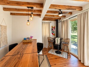 Ein Essbereich mit Holztisch, Stühlen, Pendelleuchten und Blick ins Freie durch große Fenster.