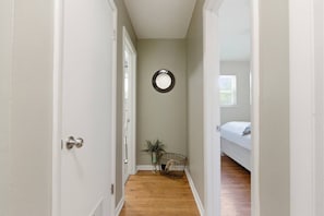 A narrow hallway with a door on the left, a small plant and basket on the floor, and a bed in the adjacent room. - Raven`s House - Fence, Garage | 10 Min. to Stadium (Columbia)
