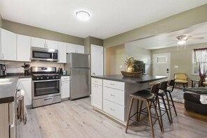 A modern kitchen with stainless steel appliances, a central island with bar stools, and a dining area with a sofa and chairs. - Raven`s House - Fence, Garage | 10 Min. to Stadium (Columbia)