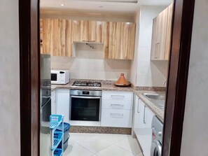 A compact kitchen with white cabinets, a microwave, a stove, and a washing machine.