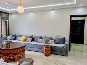 A modern living room with a grey sofa, patterned cushions, a wooden coffee table, and a round side table.