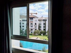 A window view of a residential building with a swimming pool, a crane, and a clear sky.
