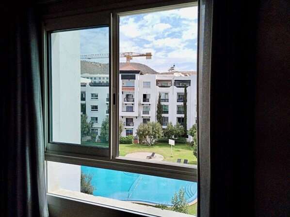 A window view of a residential building with a swimming pool, a crane, and a clear sky.