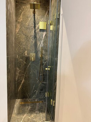 A glass-enclosed shower with a marble floor and gold fixtures. - Casa Bene Suite Rooftop Pool (Chania)