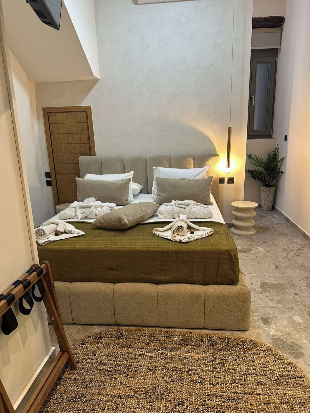 Une chambre à coucher avec un lit, des oreillers, une table de chevet, une lampe, une plante et une porte.