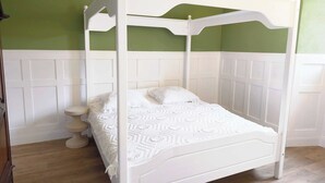 Una cama con dosel blanco, con cubrecolcha blanco, en una habitación con paredes verdes y paneles blancos.