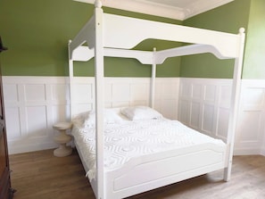 Ein weißes Himmelbett mit weißer Bettdecke in einem Zimmer mit grünen Wänden und weißem Wandverkleidung.