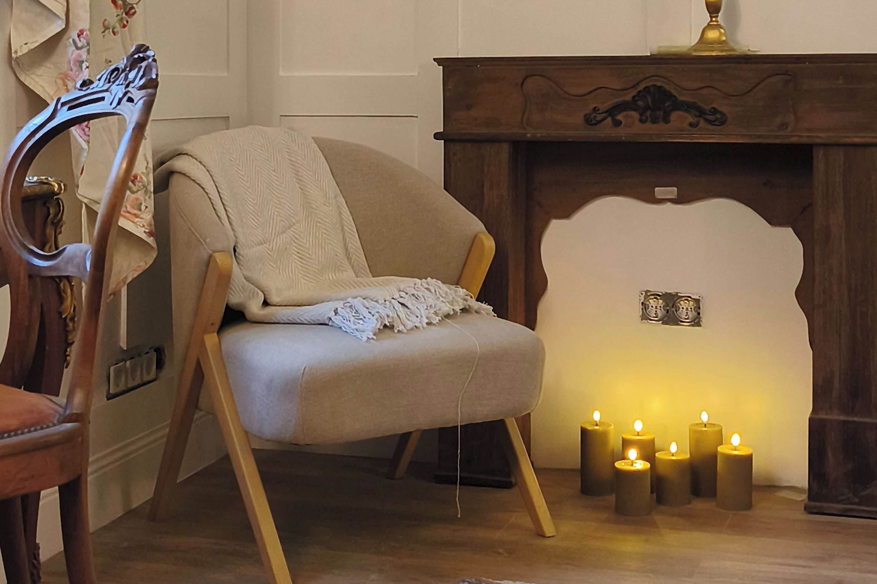A cozy room with a wooden chair, a fireplace with lit candles, and a decorative wall piece.