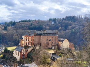 Ein großes, historisches Gebäude mit mehreren Flügeln und einem zentralen Innenhof, umgeben von bewaldeten Hügeln.