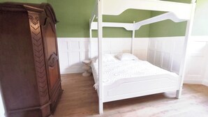 Una cama con dosel con estructura blanca y un armario de madera a la izquierda.
