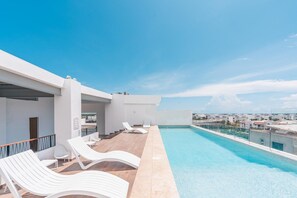 Piscina no terraço com espreguiçadeiras e vista desimpedida da paisagem urbana.