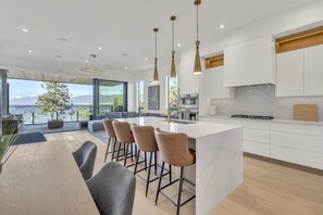 A modern kitchen with a large island, bar stools, and a view of the sea. - Lakeshore Luxury 3BR+Flex Space | Beachfront Condo (Penticton)