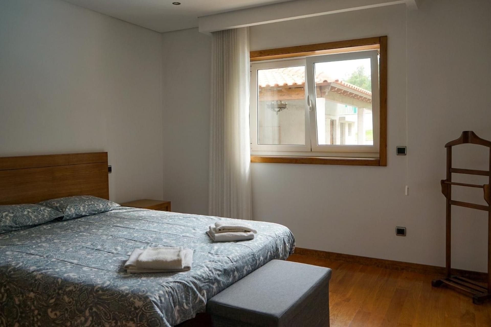 Une chambre à coucher avec un lit, une fenêtre, un banc en bois et une étagère fixée au mur.