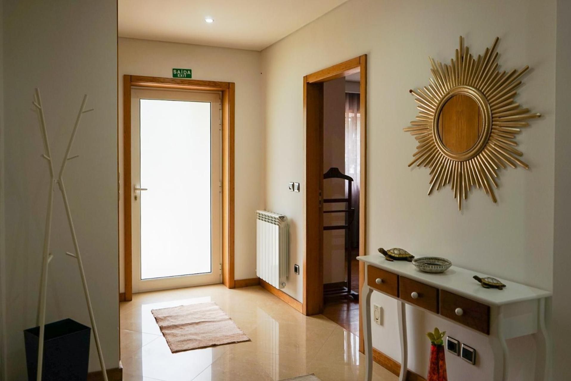 A hotel hallway with a radiator, a sunburst wall decoration, a door marked 'SAIDA EXIT', and a small table with decorative items.