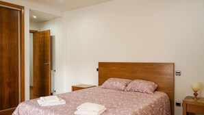 Habitación de hotel con cabecera de madera, una cama con colcha estampada, dos mesitas de noche y un tocador con lámpara.