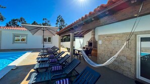 Un área junto a la piscina con sillones de descanso, una hamaca y una parrilla.