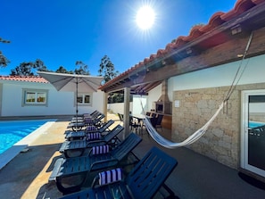 A poolside area with lounge chairs, a hammock, and a barbecue grill.