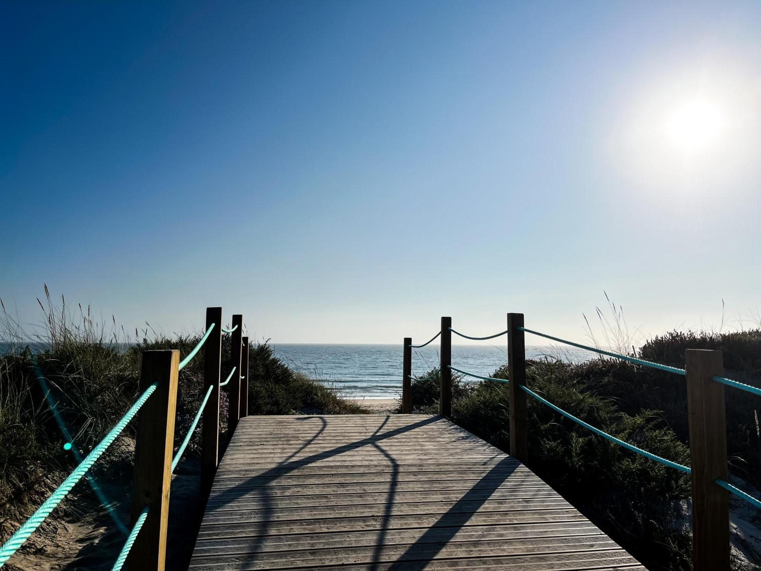 A wooden boardwalk leading to a beach with a clear sky.