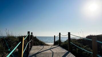 A wooden boardwalk leading to a beach with a clear sky.