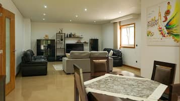 A living room with a sofa, a dining table with chairs, a TV, and a bookshelf.