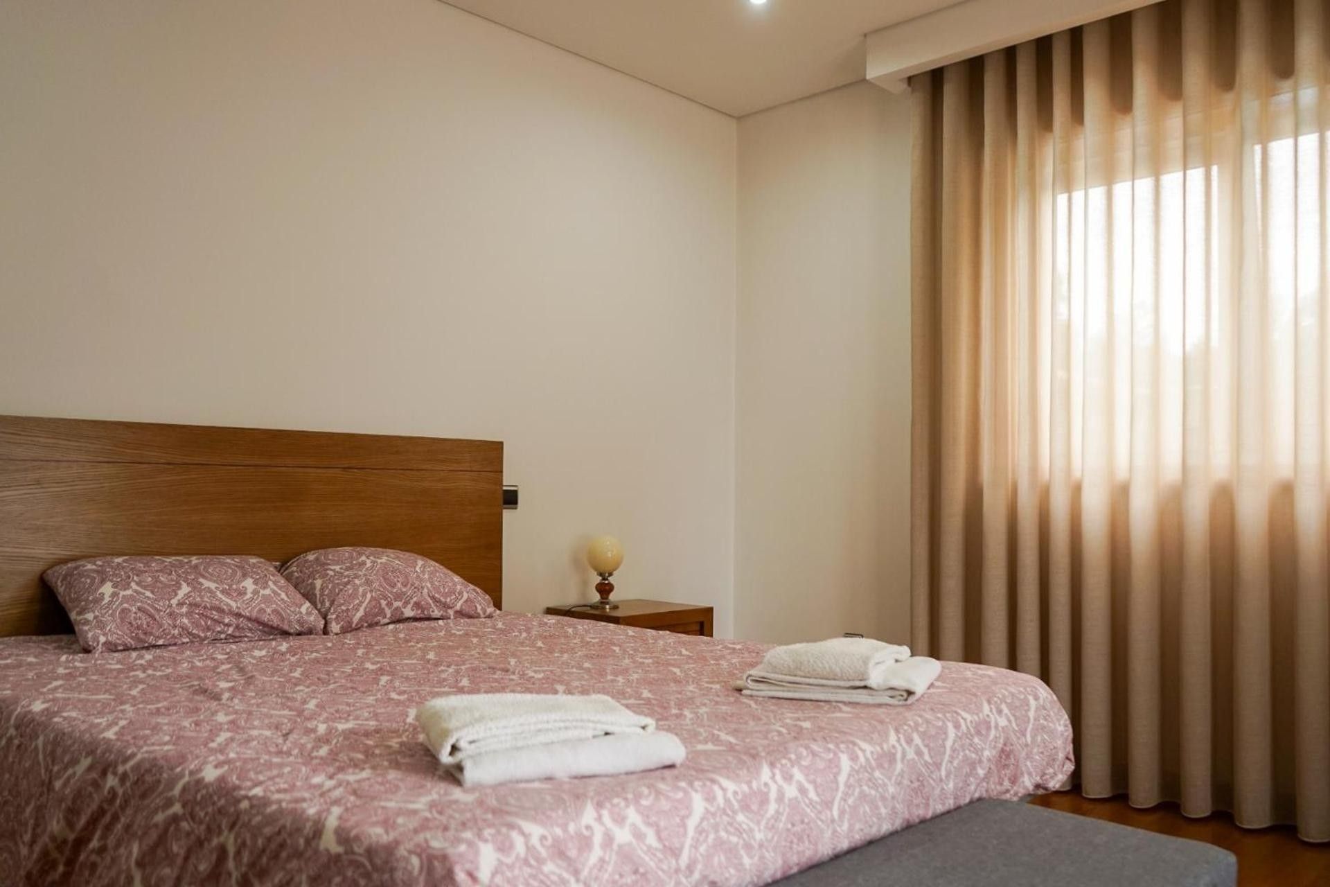 Habitación de hotel con cama, almohadas, mesita de noche, lámpara y ventana con cortinas.