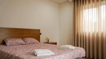 A hotel room with a bed, pillows, a nightstand, a lamp, and a window with curtains.